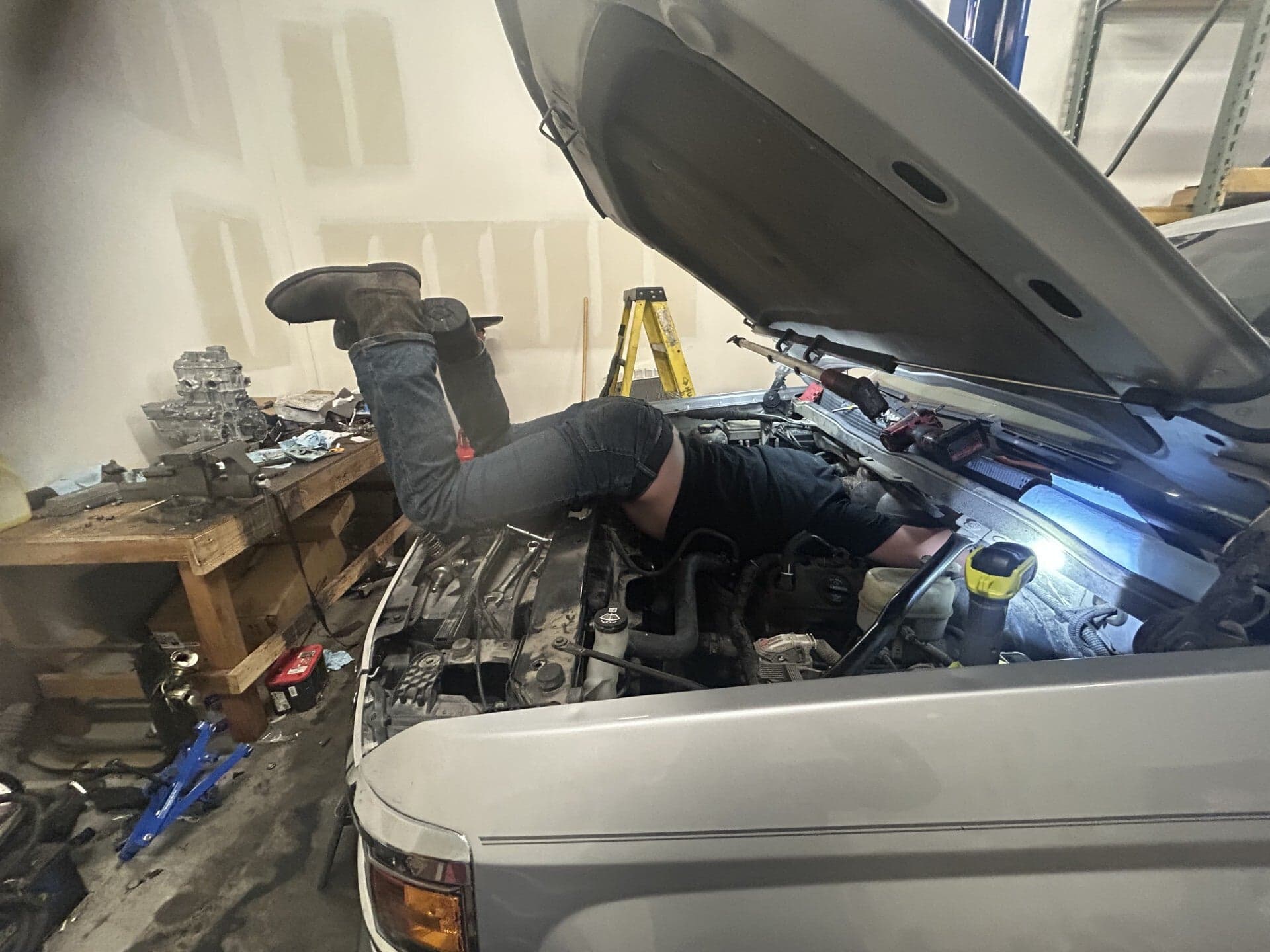 Mechanic leaning head-first into the engine bay of a silver pickup in the shop