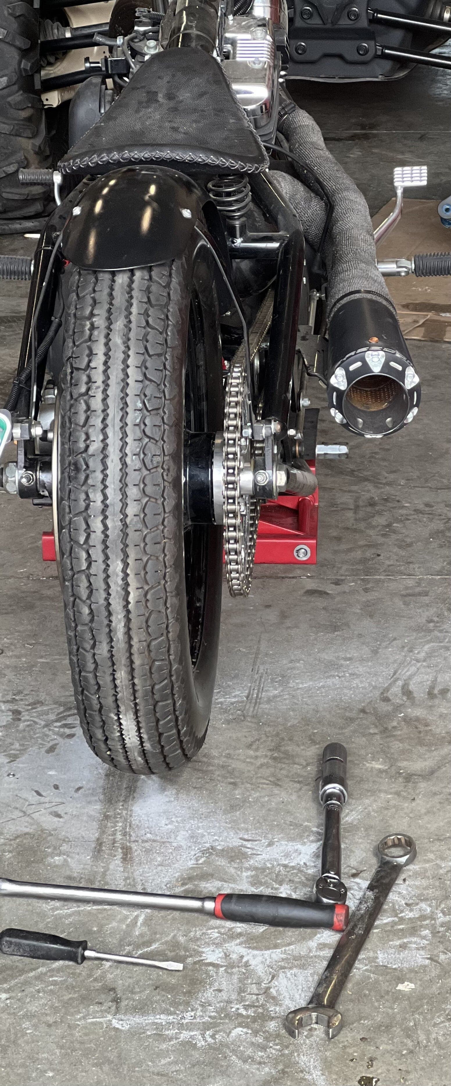 Rear wheel, chain and exhaust of a black motorcycle in the shop, with tools on the floor