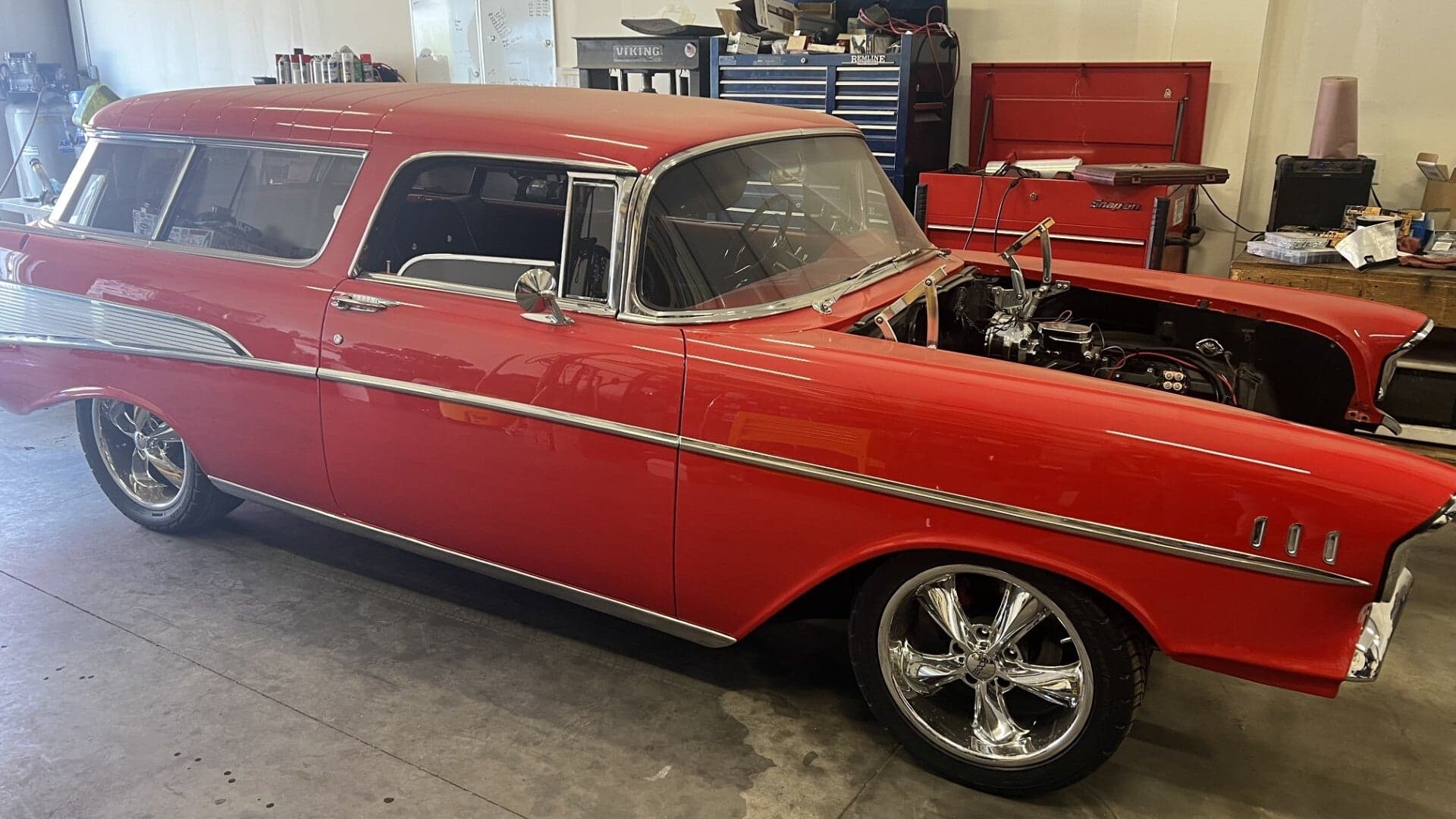 Red 1957 Chevy Nomad wagon with its hood up inside Curran’s Garage